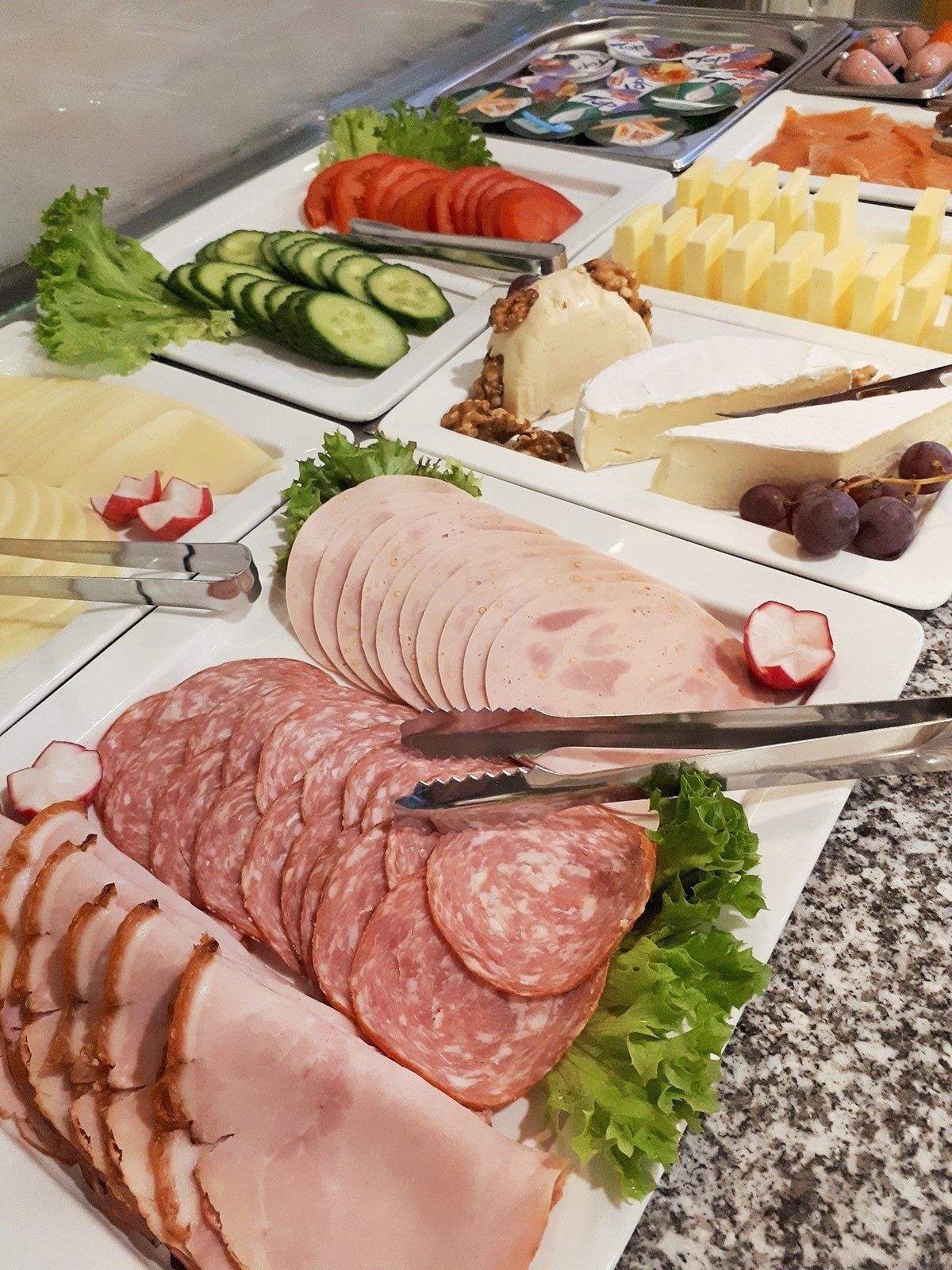 A buffet with various food items including sliced meats, cheese, and vegetables.