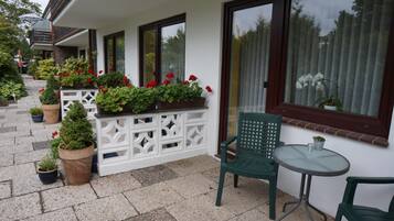 Un espace extérieur abrité, agrémenté de plantes en pot, d’une chaise verte et d’une petite table.