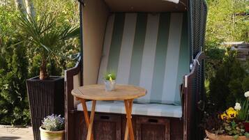 A wicker outdoor seating area with a cushioned bench, a small round table, and potted plants.