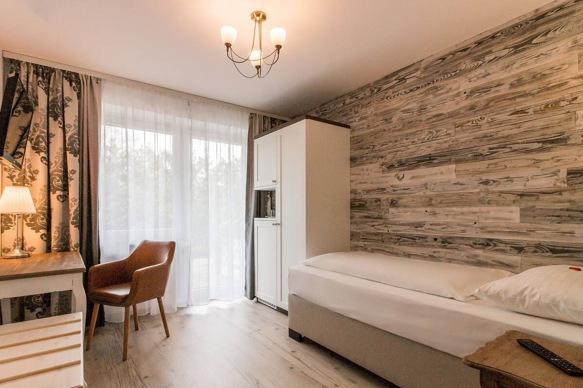 A hotel room with a bed, a desk with a lamp, a chair, and a wardrobe.