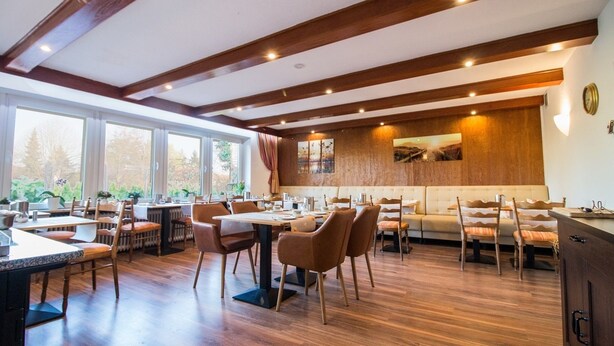 Un restaurante con vigas de madera, ventanas amplias y una combinación de mesas y cabinas.