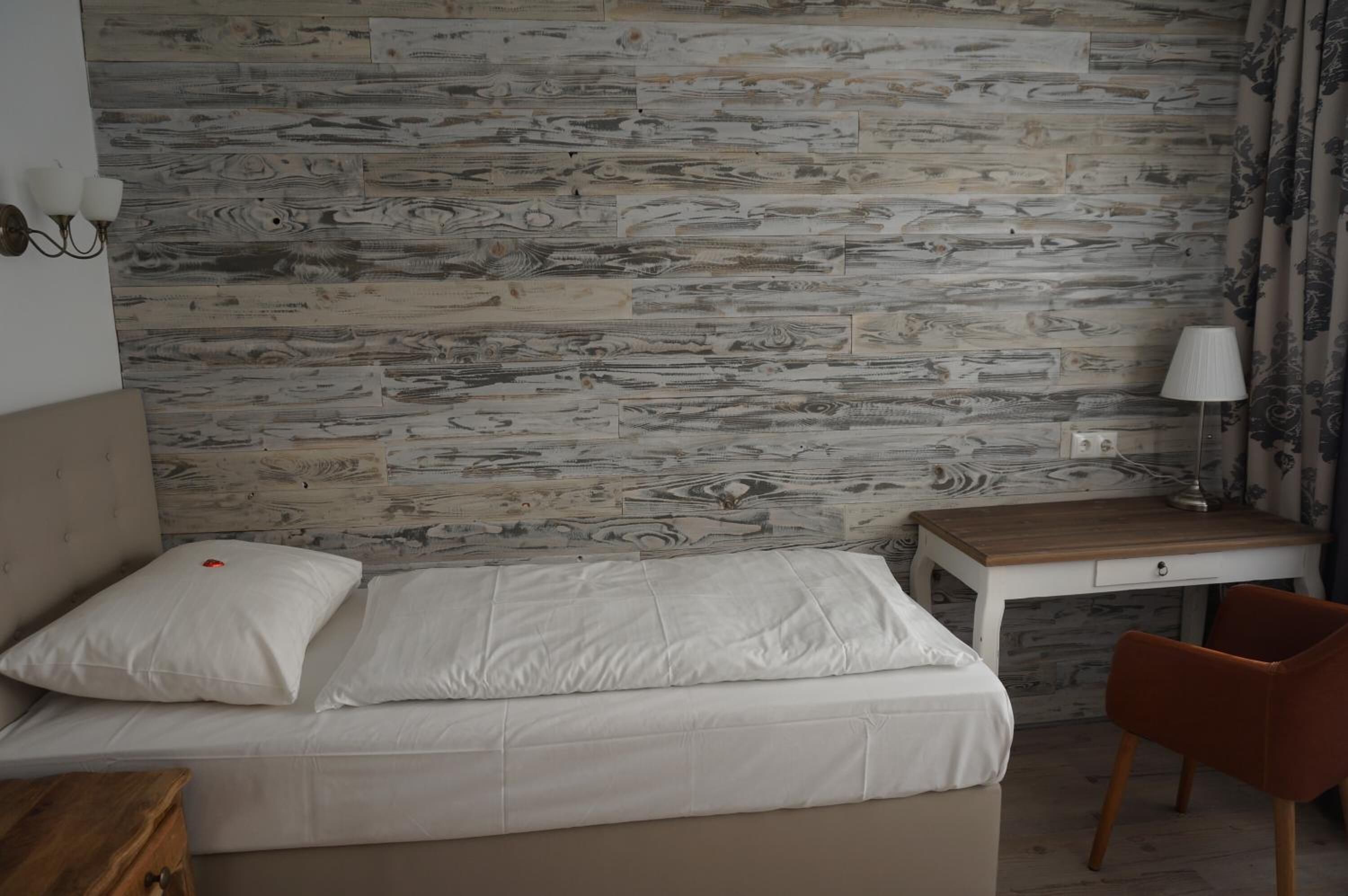 A bedroom with a bed, a wooden nightstand, a desk, and a chair.