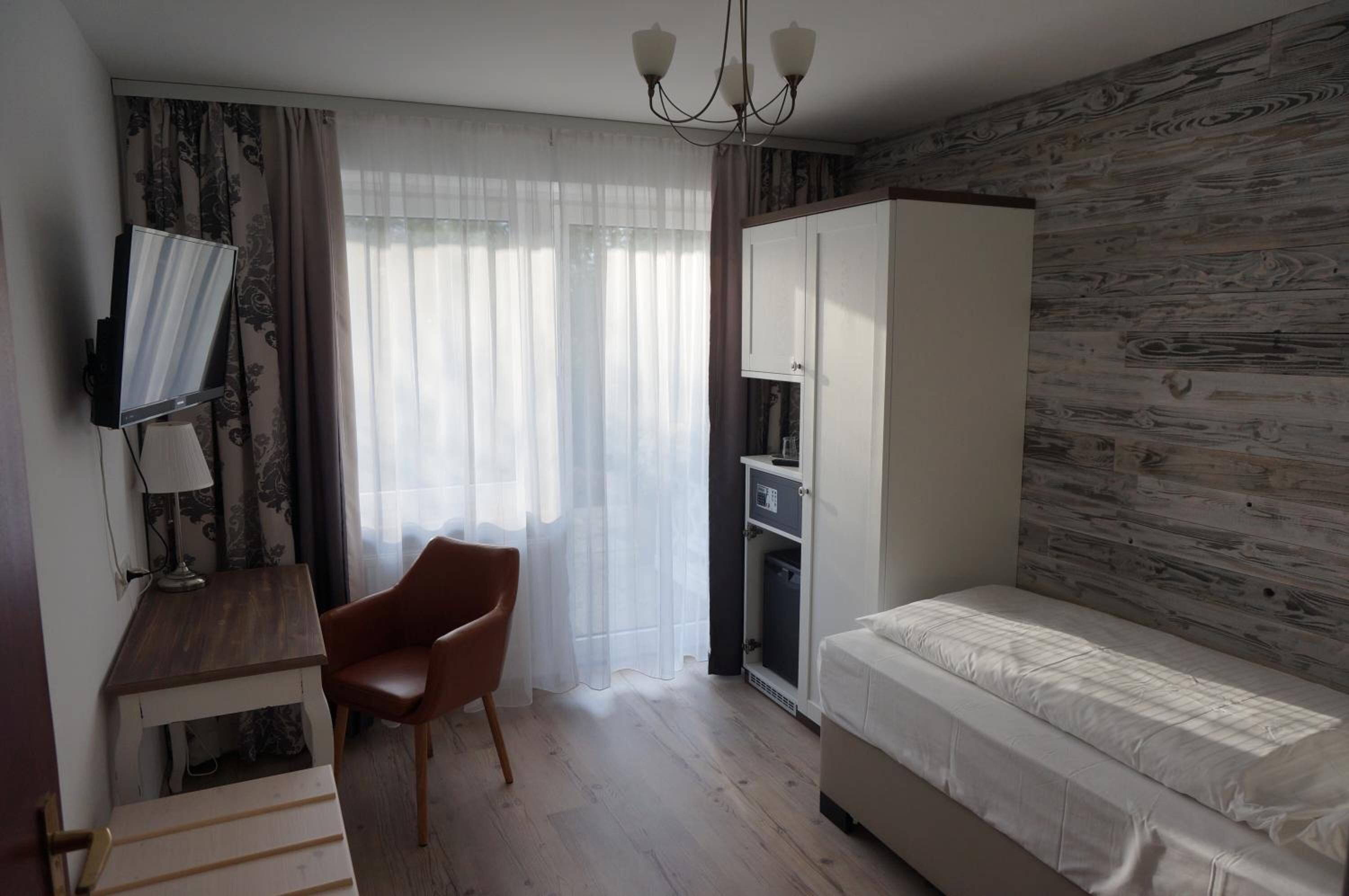 Een slaapkamer met een bed, een bureau met stoel, een televisie, een kledingkast en een raam met gordijnen.