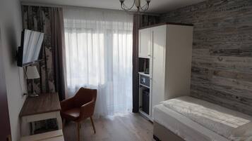 Een slaapkamer met een bed, een bureau met stoel, een televisie, een kledingkast en een raam met gordijnen.