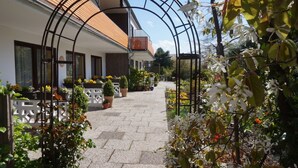 Un sendero conduce a un edificio con techo de tejas, rodeado de macetas con plantas y flores.