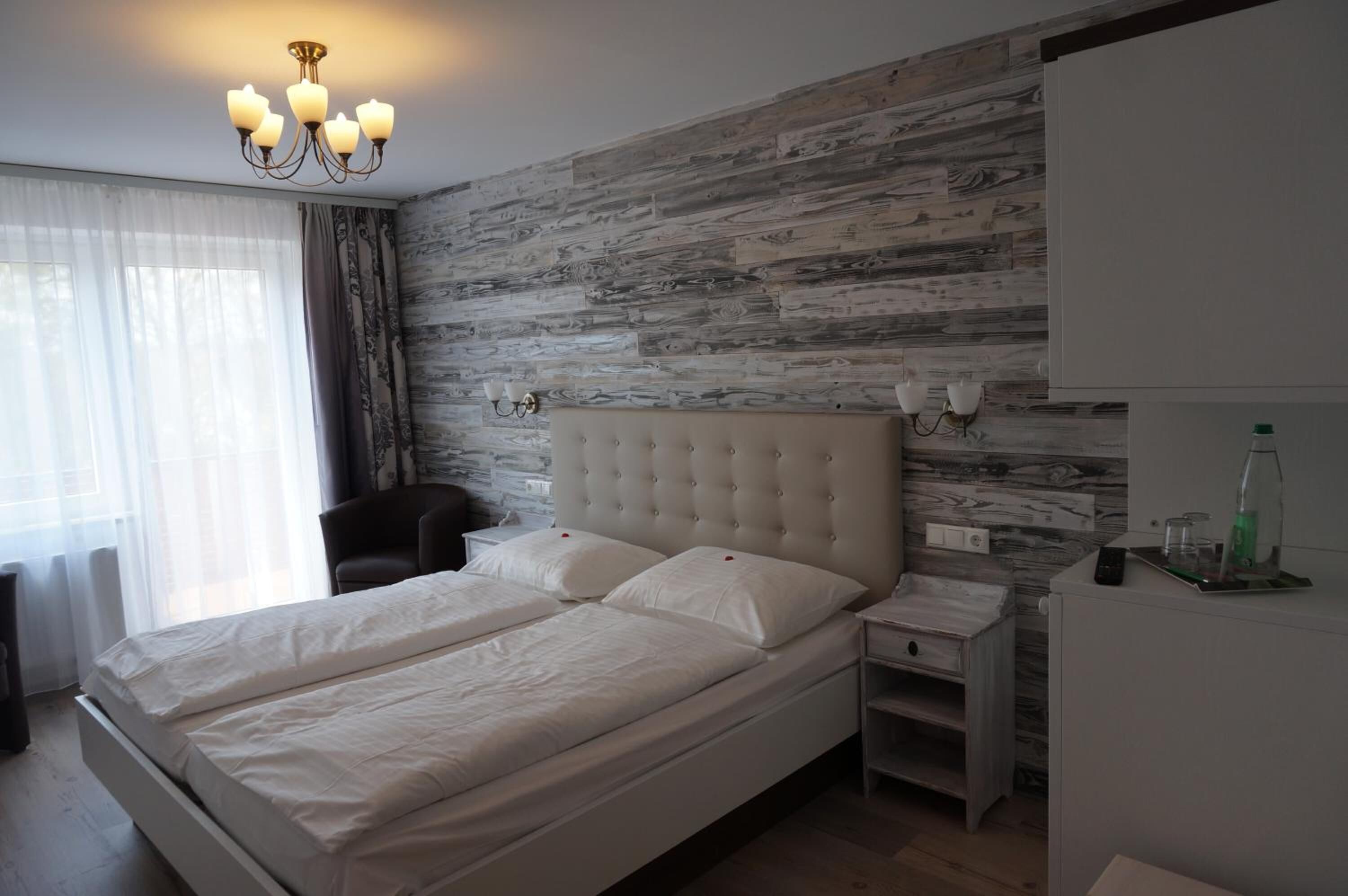 A bedroom with a large bed, bedside tables, a chair, a wardrobe, and a chandelier.