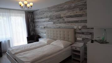 A bedroom with a large bed, bedside tables, a chair, a wardrobe, and a chandelier.