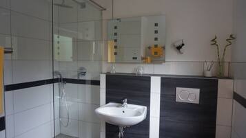Un bagno moderno con cabina doccia in vetro, lavandino bianco e uno specchio grande sopra il lavandino.