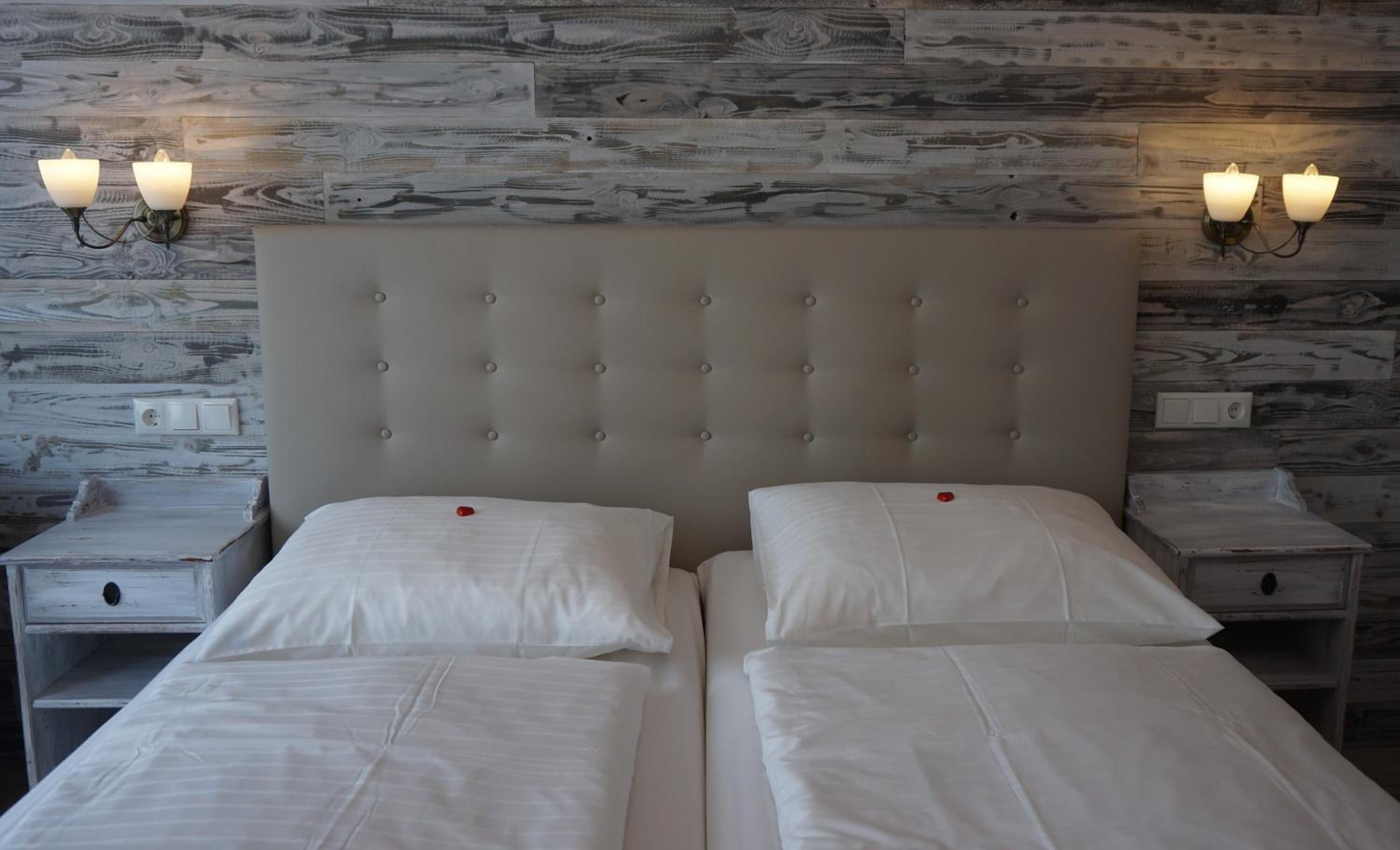 A double bed with a tufted headboard, two bedside tables with wall-mounted lamps, and a wooden wall with a distressed finish.