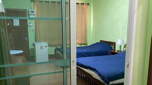 A room with a bed, a desk, a chair, a small table, a lamp, and a sliding door. - Kanoktid Place (Fang)