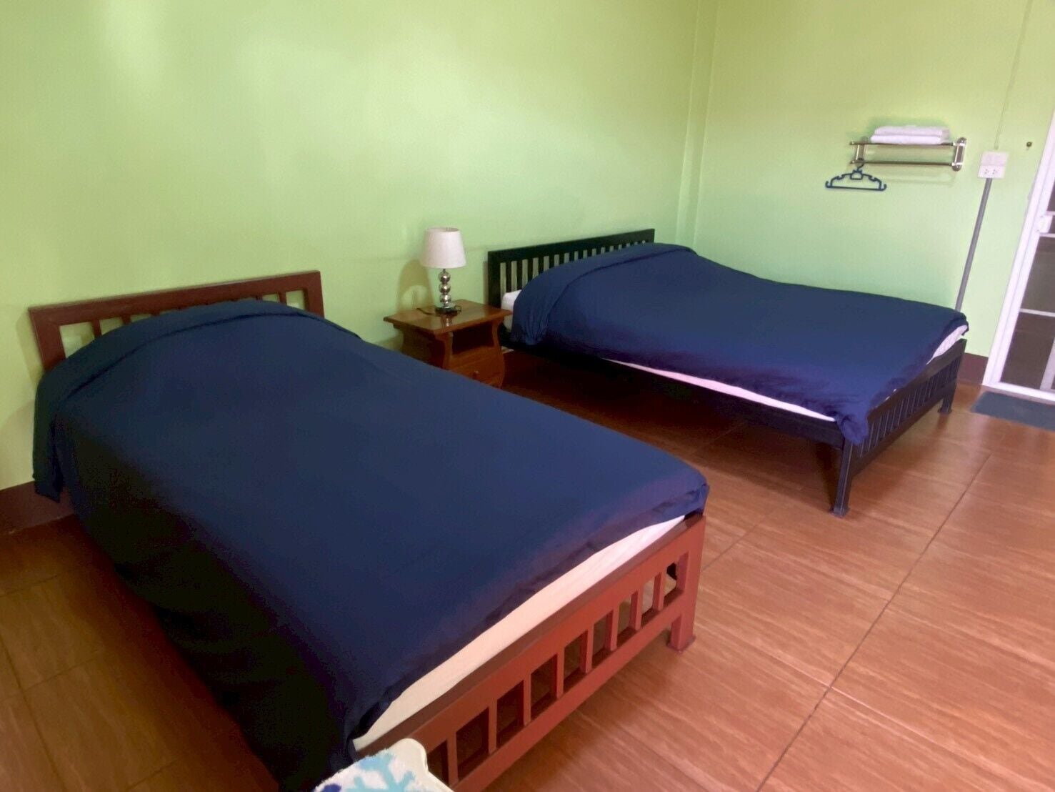Una habitación con dos camas, una mesita de noche con lámpara y un perchero en la pared.