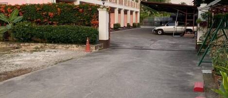 A building with a covered walkway, a parked vehicle, and a garden area.