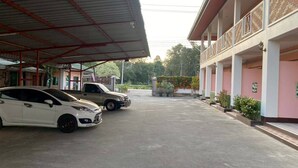 A parking area with two cars, a covered walkway, and a building with a pink facade and balconies. - Kanoktid Place (Fang)