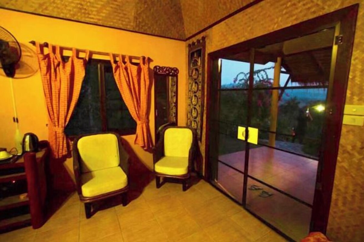 A room with two chairs, a fan, a window with curtains, and a sliding glass door leading outside.