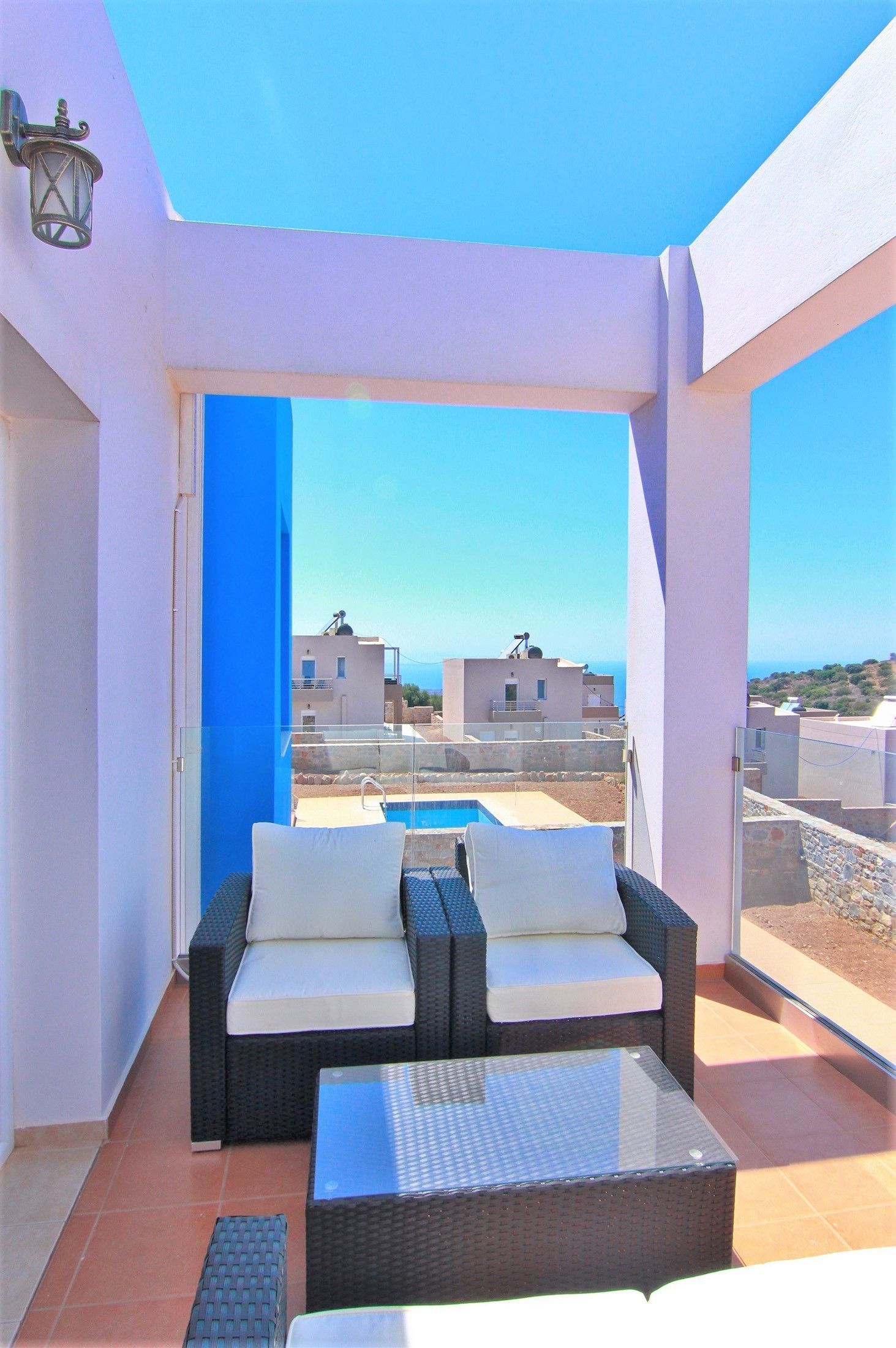A balcony with a sofa and a table, overlooking a pool and buildings.