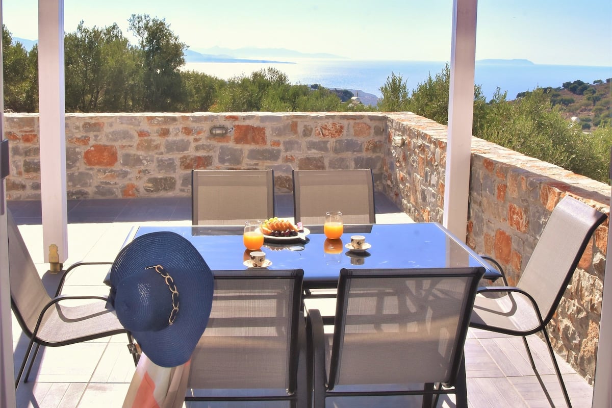 Une terrasse extérieure avec une table et des chaises, un ventilateur et une vue sur la mer.