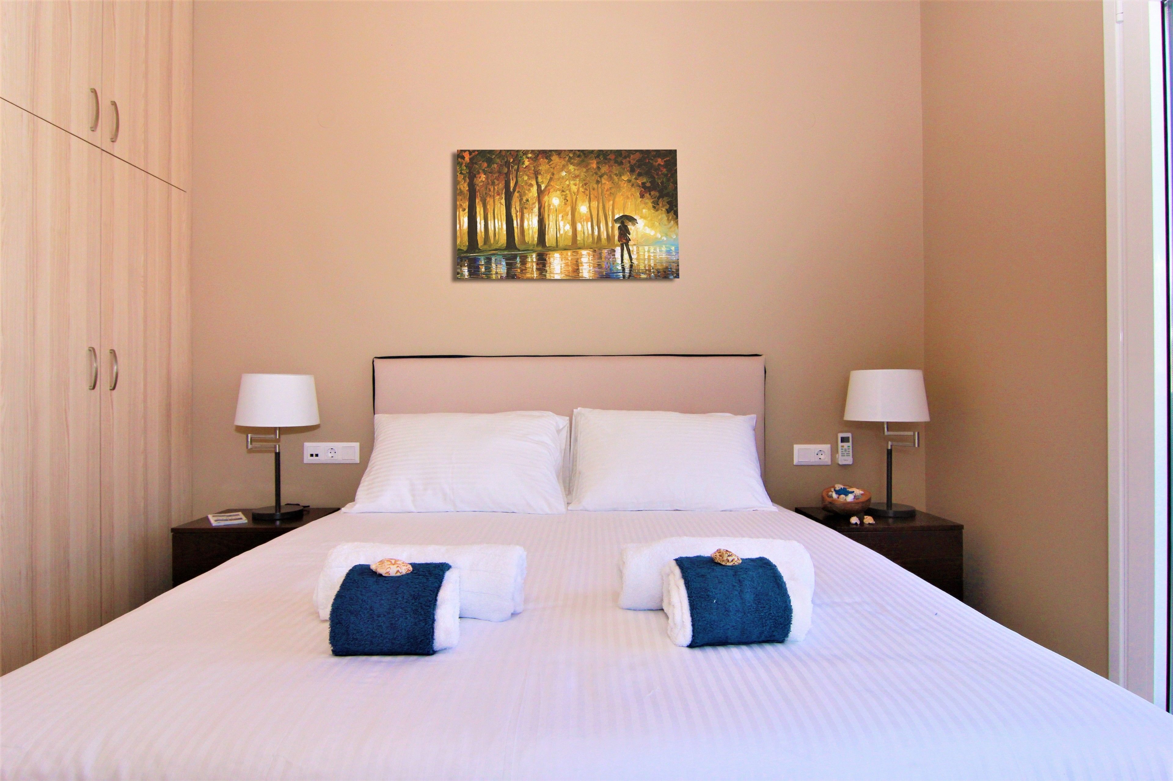 Een hotelkamer met een groot bed, twee nachtkastjes met lampen, een schilderij aan de muur en een kledingkast.