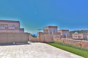 A residential area with modern buildings, a paved courtyard, and a stone wall with flowers.