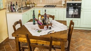 Eine Küche mit hellgrünen Schränken, einer gefliesten Spritzschutzwand, einem Holzesstisch mit Stühlen und verschiedenen Flaschen und Gläsern auf der Arbeitsplatte.