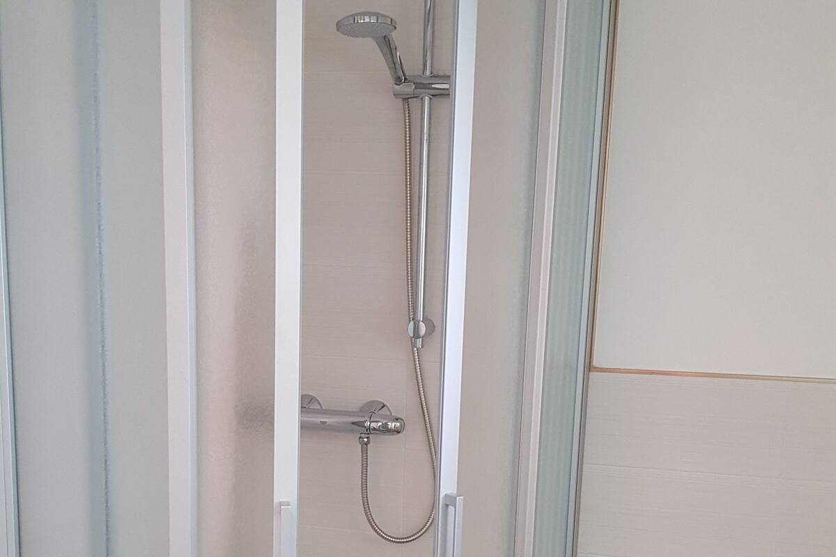 A glass-enclosed shower stall with a handheld showerhead and a fixed showerhead.
