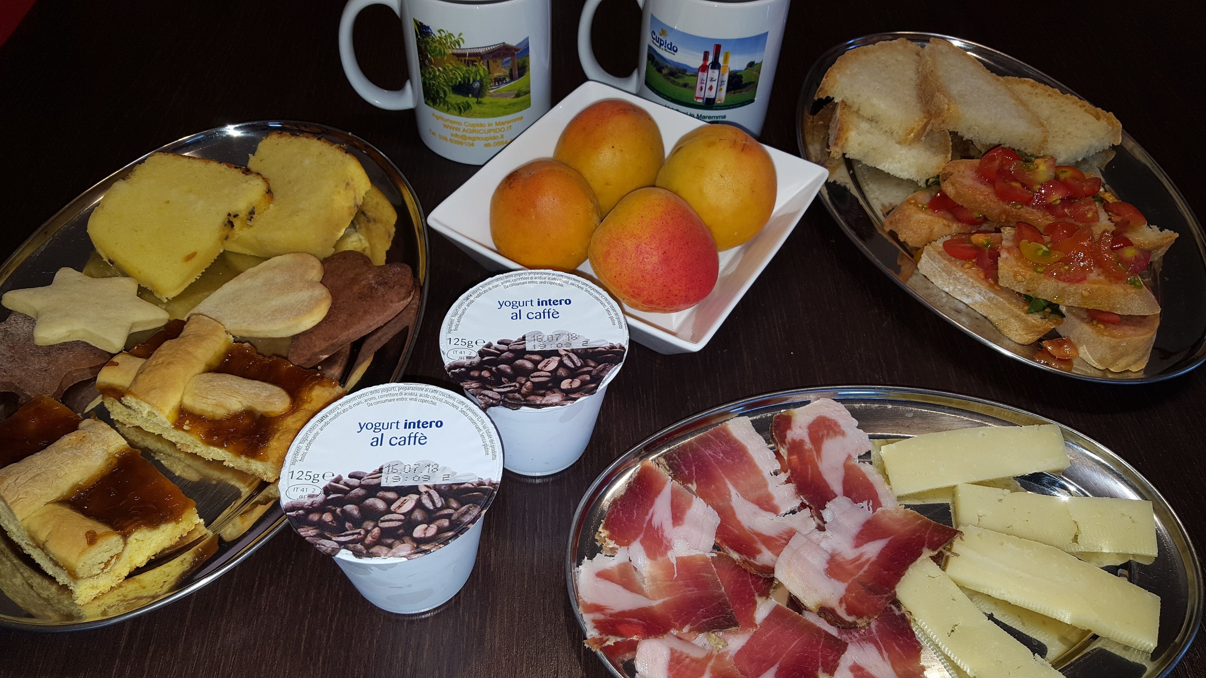 Ein Tisch mit verschiedenen Speisen, darunter Brot, Obst, Käse und Fleisch.
