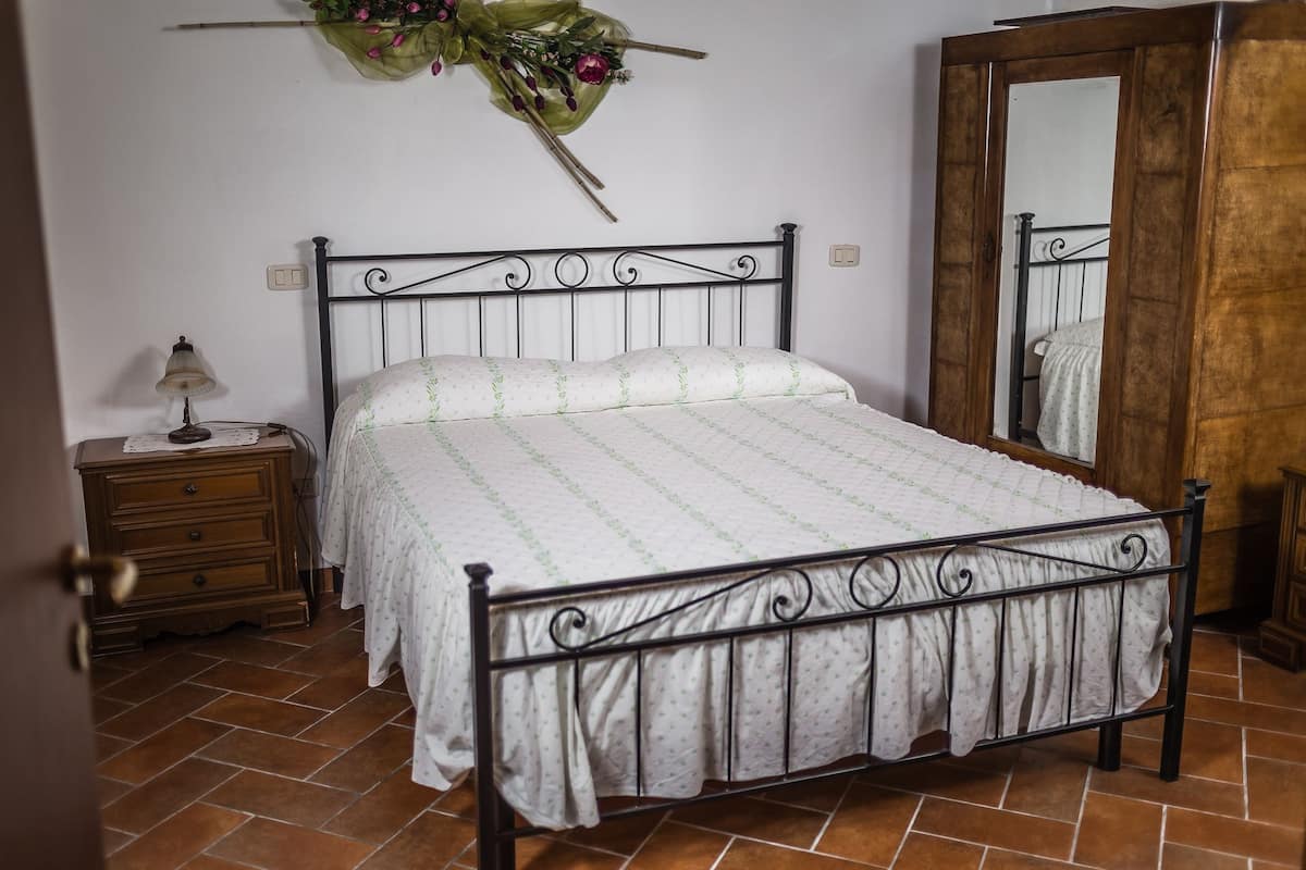 A bedroom with a bed, a nightstand, a lamp, a mirror, and a door.
