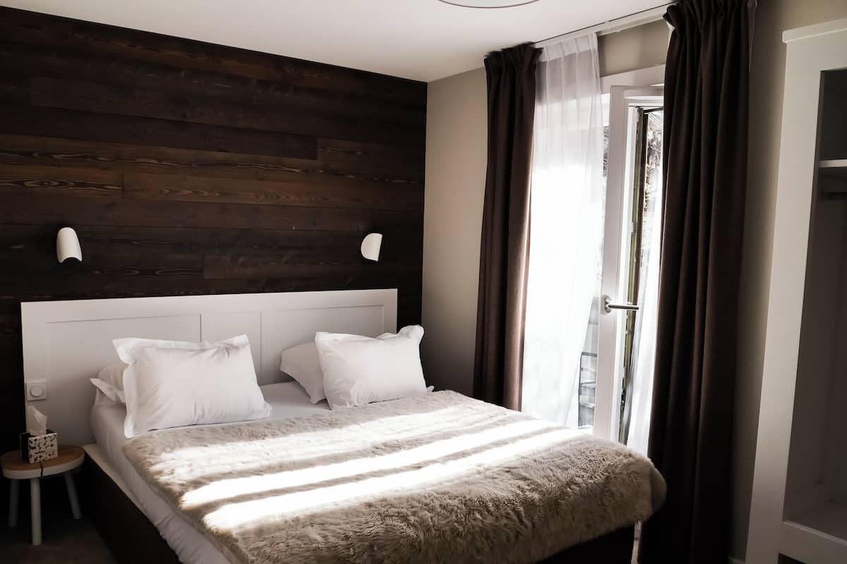 Une chambre à coucher moderne avec une tête de lit en bois, une couette blanche moelleuse et une table de chevet sur laquelle se trouve une boîte de mouchoirs.