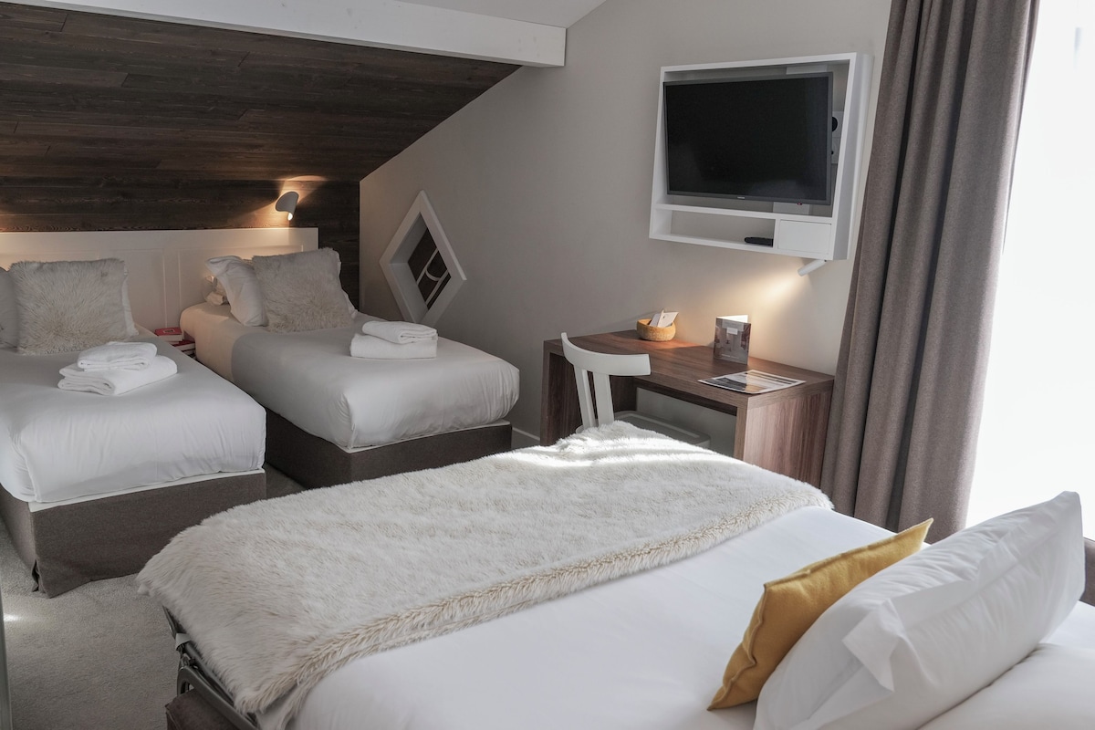 A hotel room with two beds, a TV, a desk, and a window.