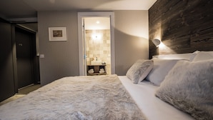 Een slaapkamer met een groot bed, een houten hoofdbord, een ingelijst schilderij aan de muur, en een badkamer zichtbaar door een open deur.