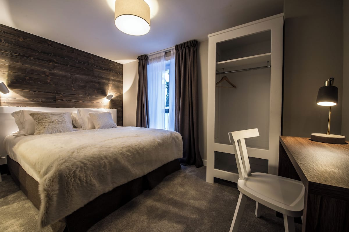 Une chambre moderne avec un grand lit, un bureau avec une chaise, une armoire et un porte-manteau.