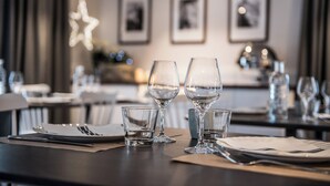 Een eettafel gedekt met wijnkansen, een klein glas en borden, met ingekaderde foto's aan de muur op de achtergrond.