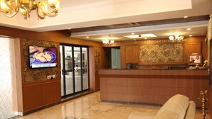Un hall de hotel con mostrador de recepción, televisor, sofá y candelabro.