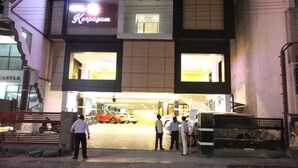 Un edificio con un cartel que dice "Karpagan" y un estacionamiento con coches y gente.
