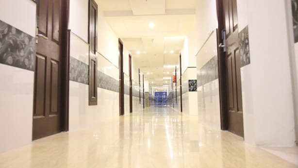Un pasillo largo y bien iluminado con piso brillante, puertas a ambos lados y una escalera al final.