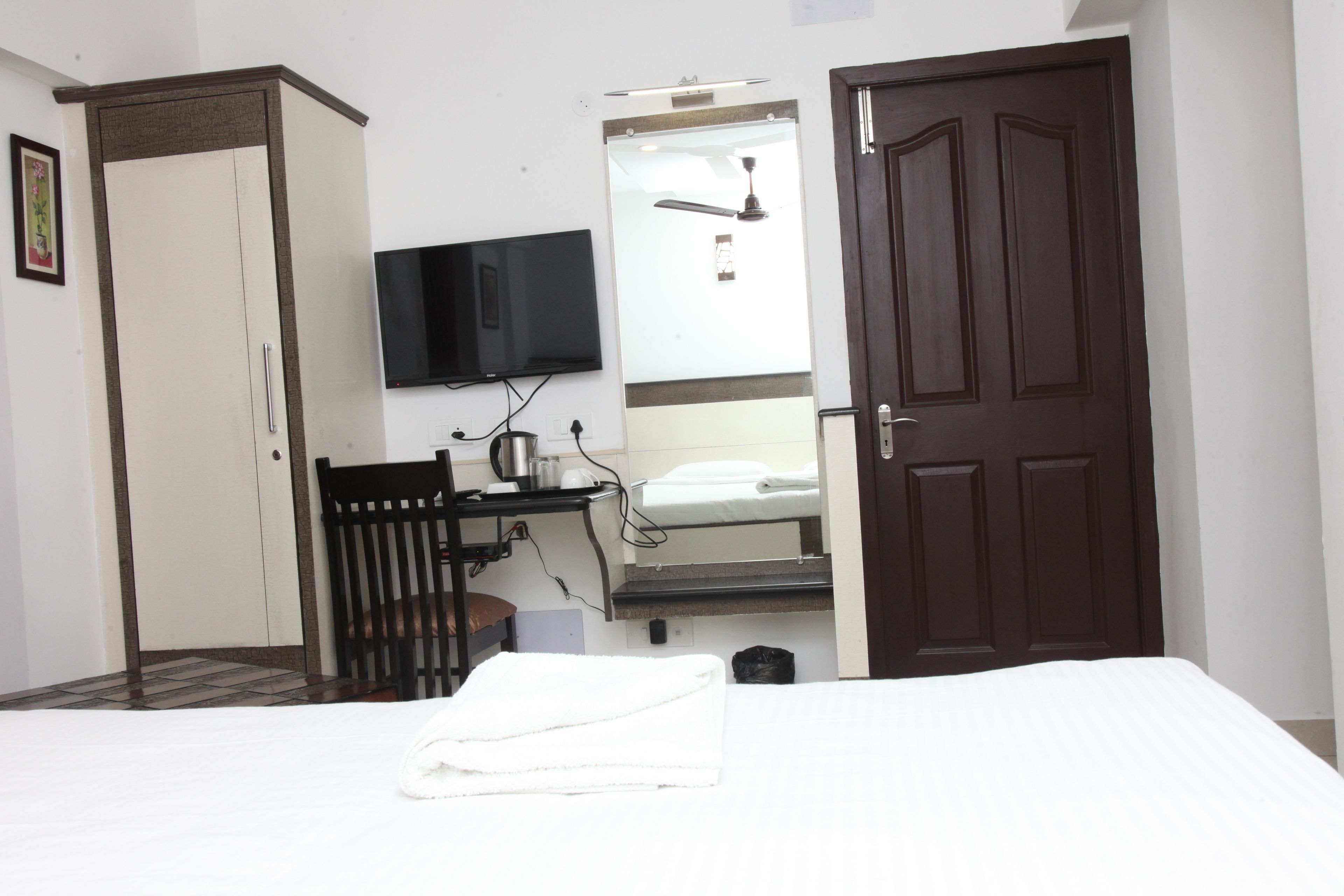 A bedroom with a bed, a wardrobe, a desk with a chair, a television, and a door.