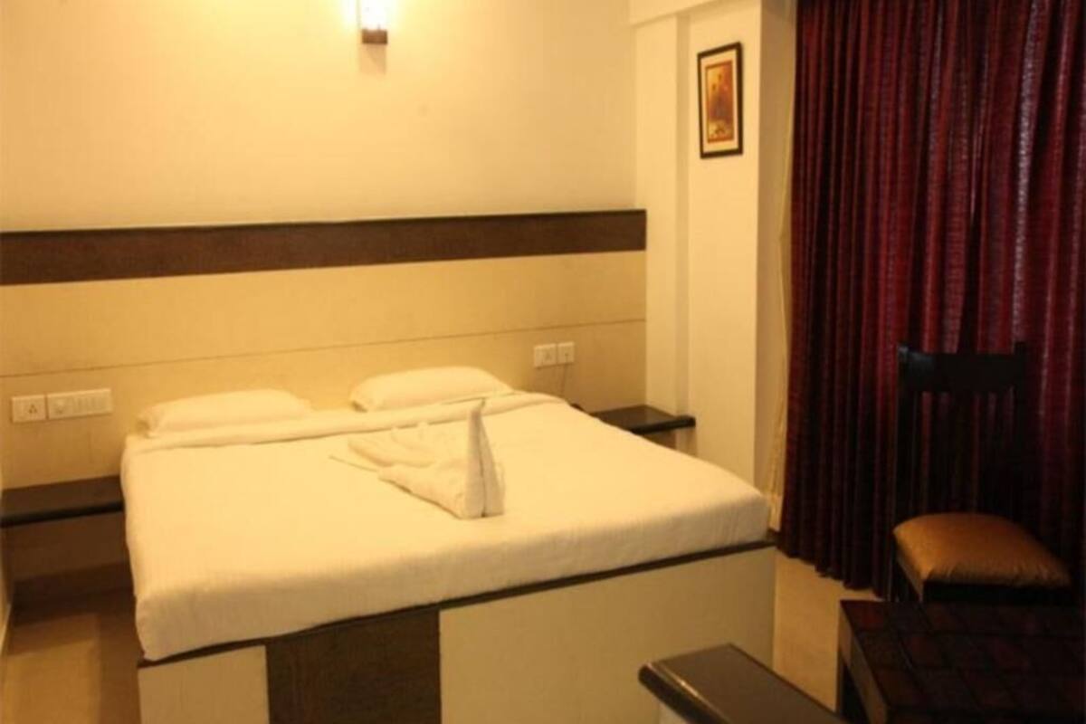Una habitación de hotel con una cama, una mesita de noche, una silla y una ventana con cortinas.