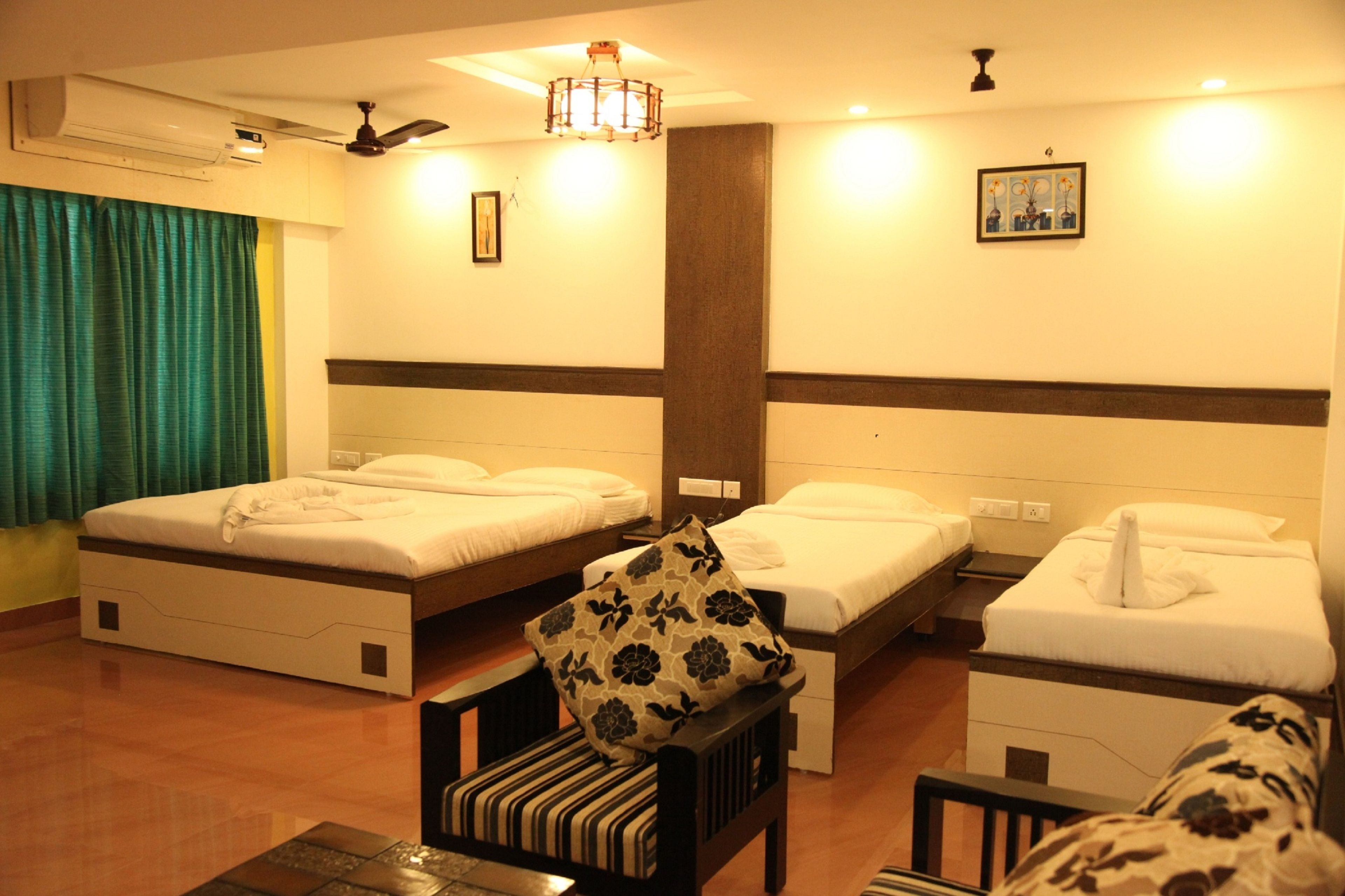 A hotel room with two single beds, a sofa, a chair, a small table, and a ceiling fan.