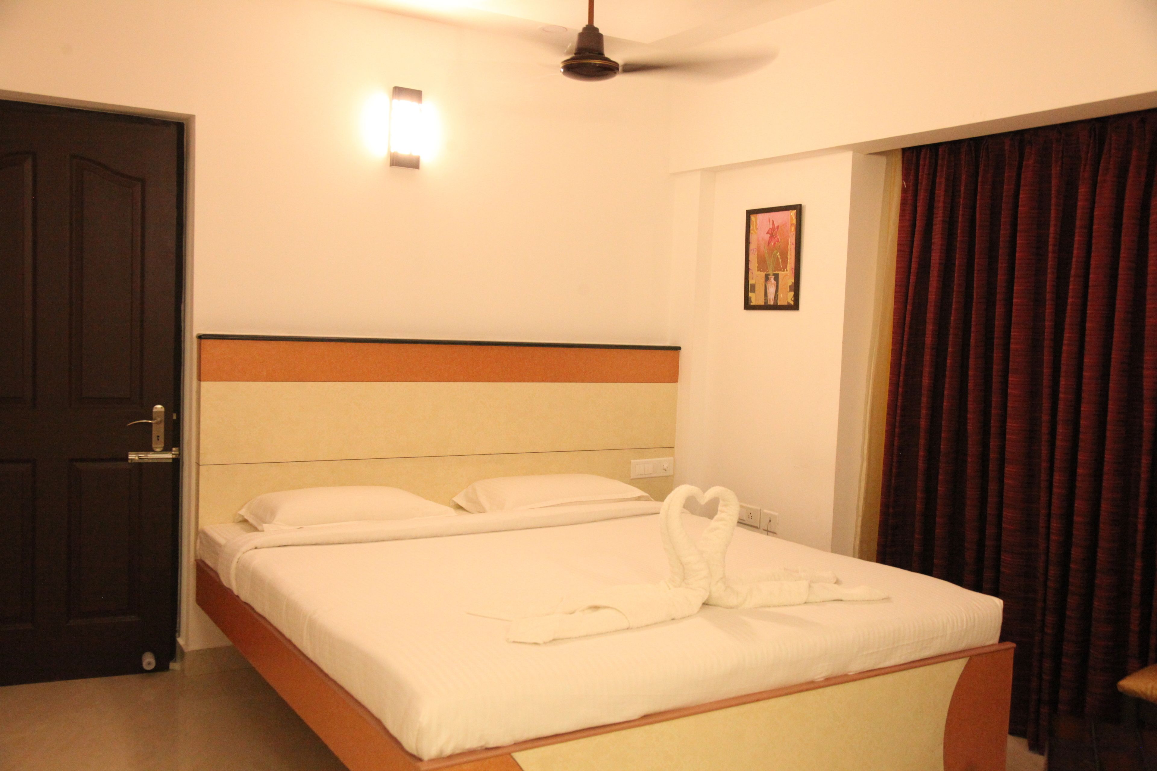 Habitación de hotel con cama, ventilador de techo, puerta y ventana con cortinas.