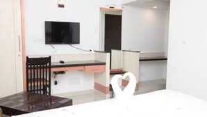 Habitación de hotel con escritorio, televisor, espejo y cama decorada con forma de corazón.