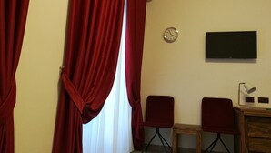 Una habitación con cortinas rojas, un reloj, dos sillas rojas y un escritorio de madera.