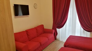 Una habitación con un sofá rojo, un televisor montado en la pared y una ventana con cortinas rojas.