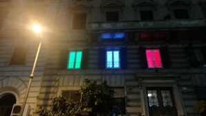 Un edificio con varias ventanas, algunas con luces de colores. Hay un farol y un árbol en primer plano.