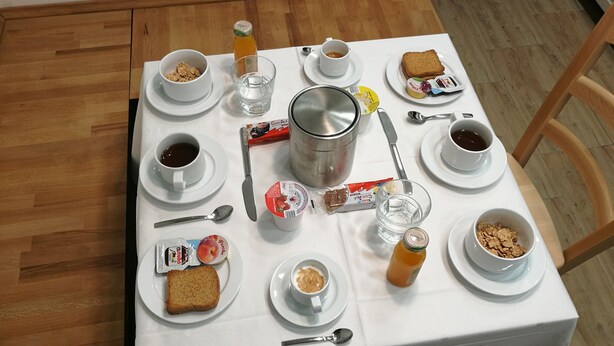 Una mesa de desayuno con diversas opciones de comida y bebidas, como tostadas, cereal, yogur y café.