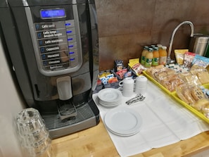 A coffee machine with various drink options, a sink, and breakfast items like bread, pastries, and condiments. - Al Trenino Accomodation (Rome)