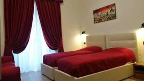 Un dormitorio con dos camas, cortinas rojas, un cuadro y una mesita de noche.