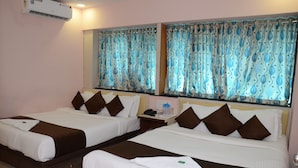 A hotel room with two beds, each with white bedding and brown pillows, a bedside table with a phone and a water bottle, and a large mirror above the beds. - Hotel Sai Leela Grand (Mumbai)