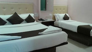 Habitación de hotel con dos camas, cada una con ropa blanca y almohadas oscuras. Hay una mesita de noche con un teléfono y una lámpara pequeña.