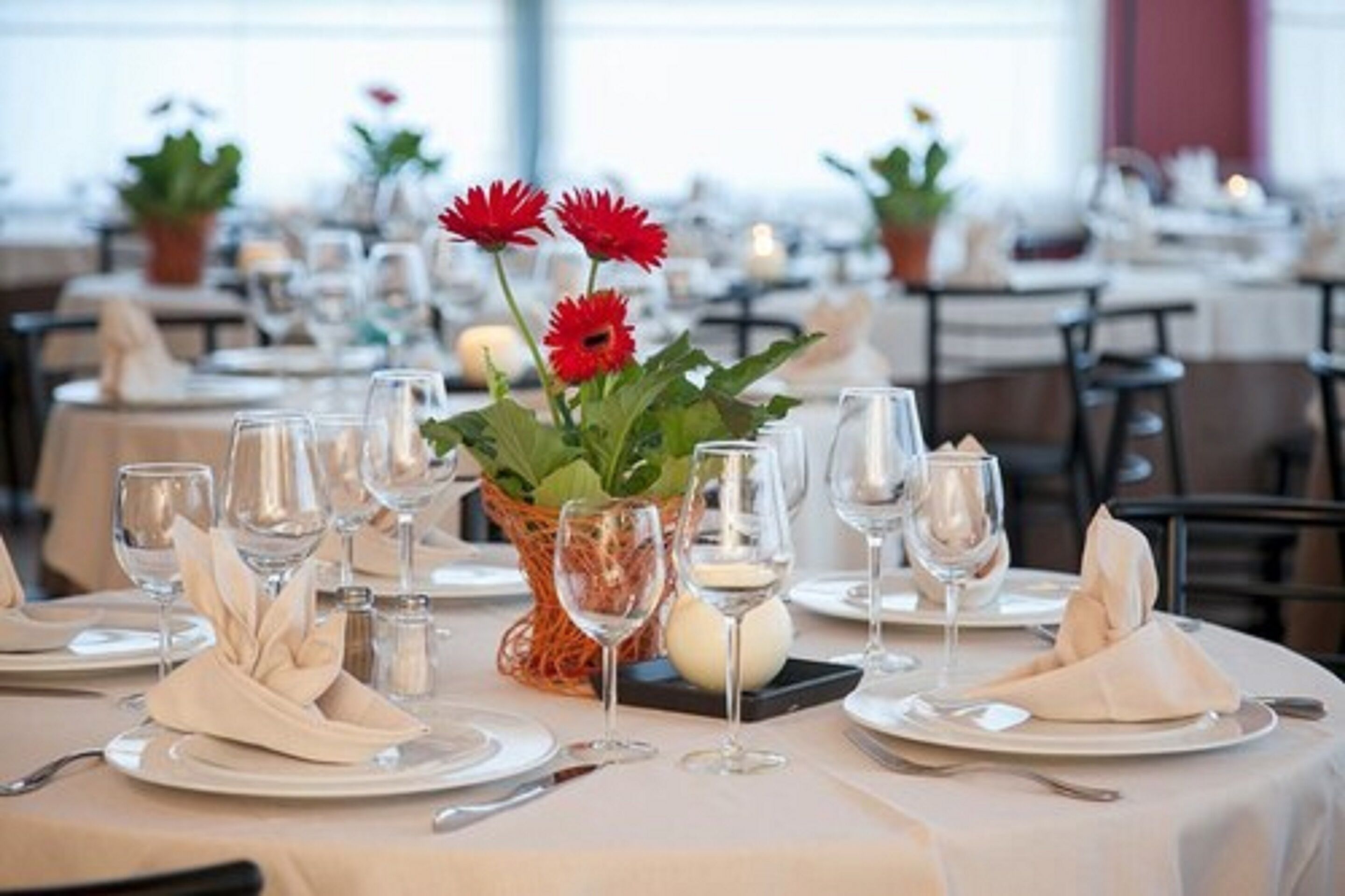 Una mesa de comedor con platos, vasos y un centro de mesa de flores rojas.