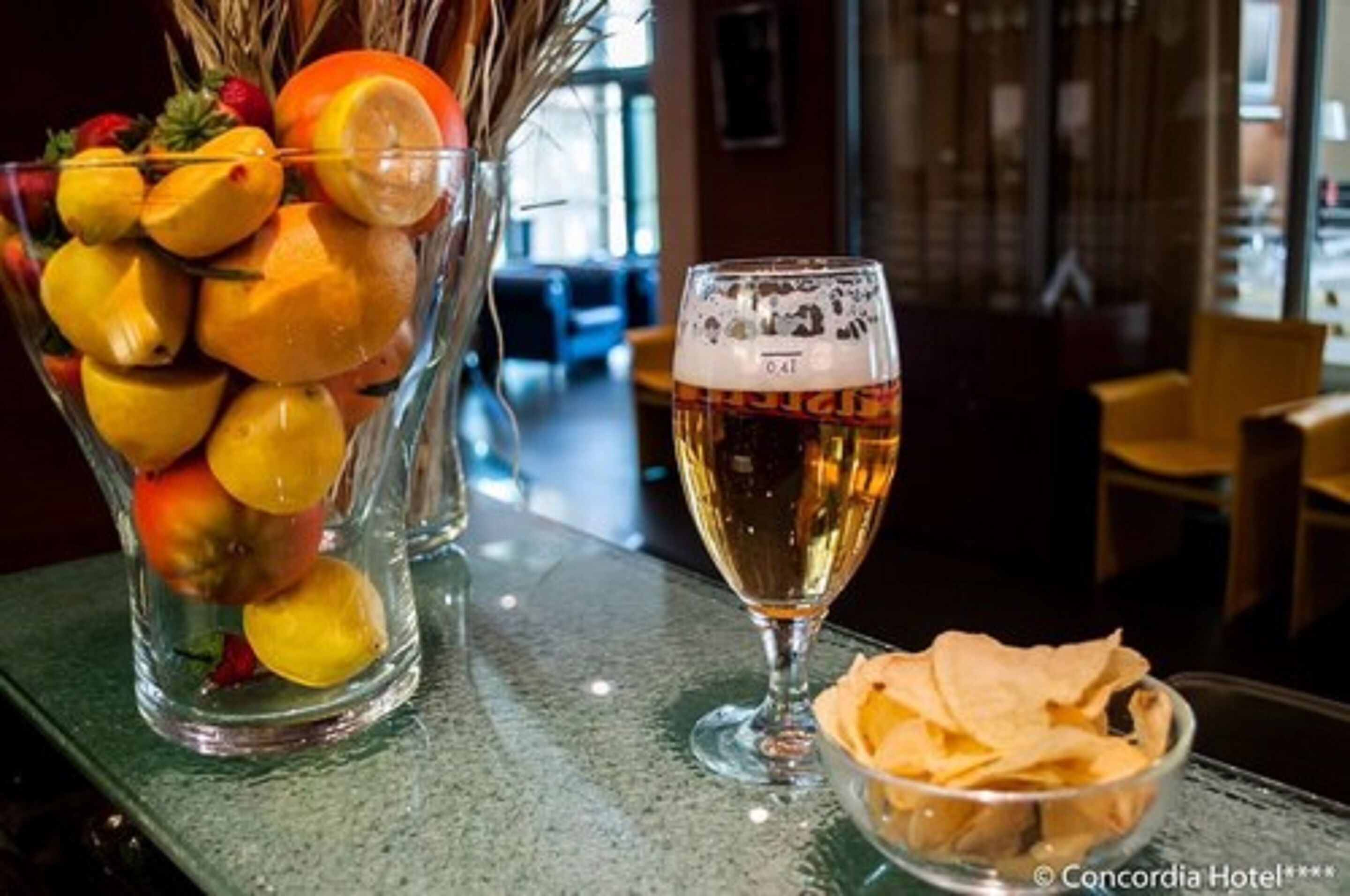 Una cerveza en la barra con un bol de papas fritas y un frutero con naranjas y limones.