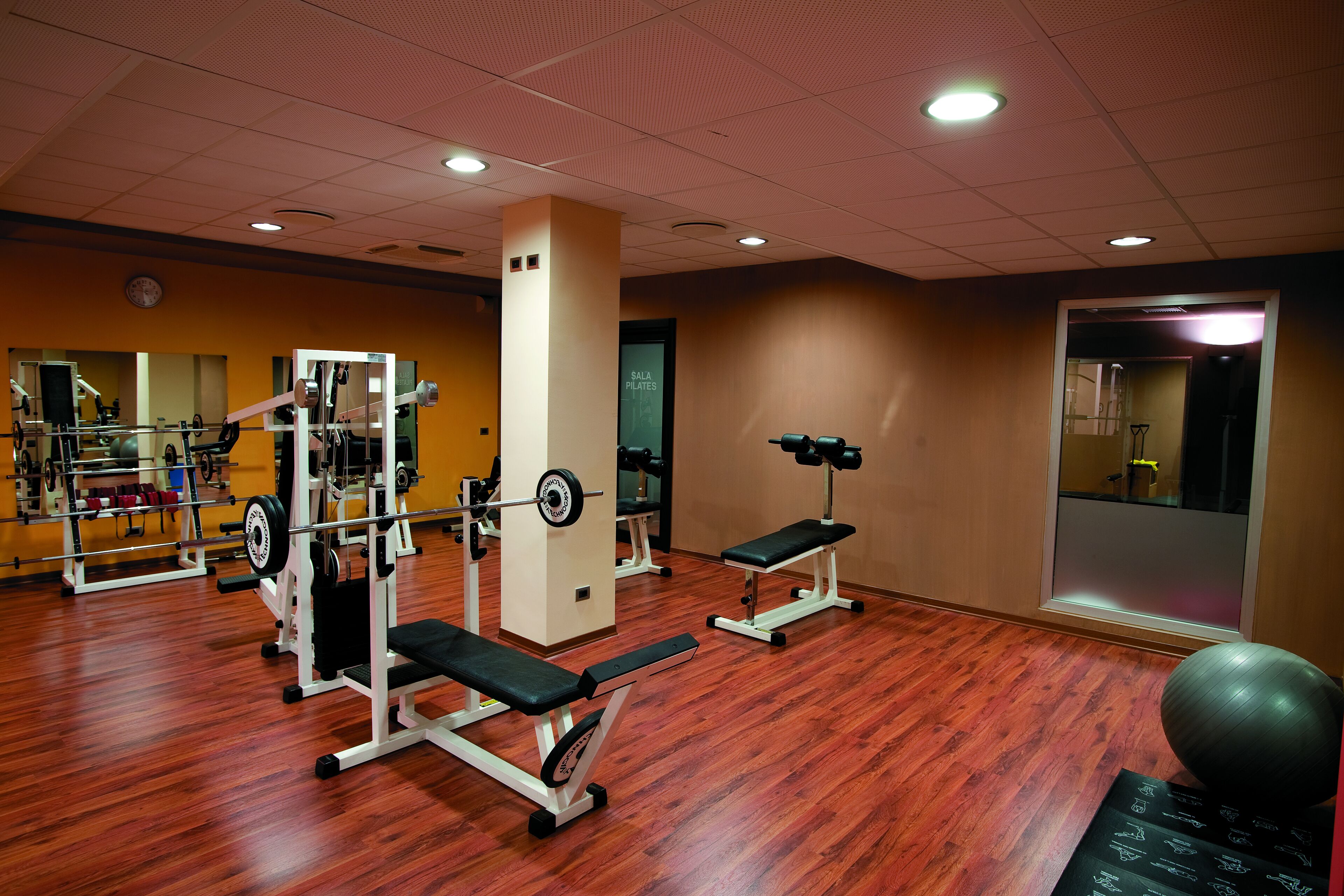 Une salle de sport équipée de matériel de musculation, de bancs et dotée d’un mur recouvert de miroirs.